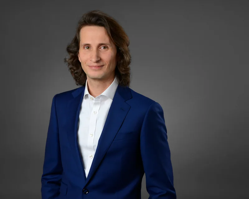 Mann mit schulterlangen Haaren in blauem Anzug