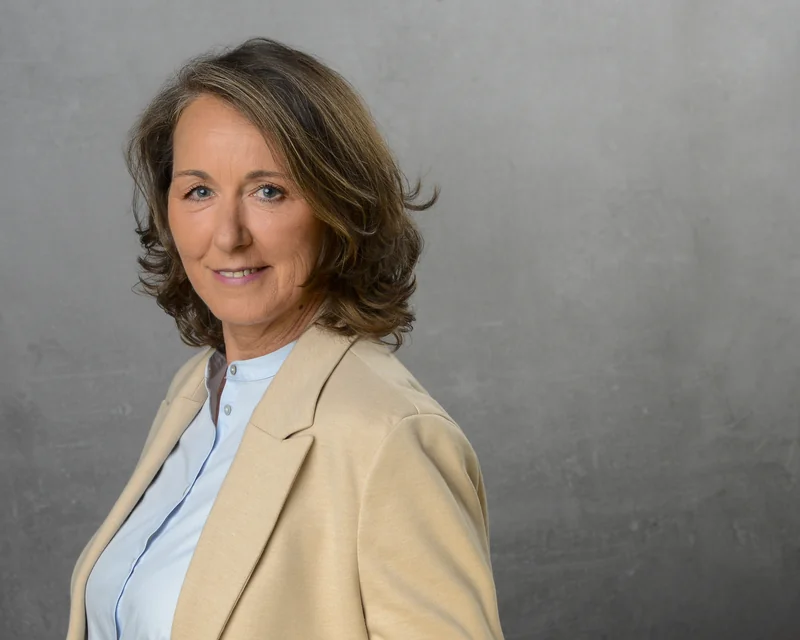 Bewerbungsportrait einer Frau in beigem Blazer und hellblauer Bluse
