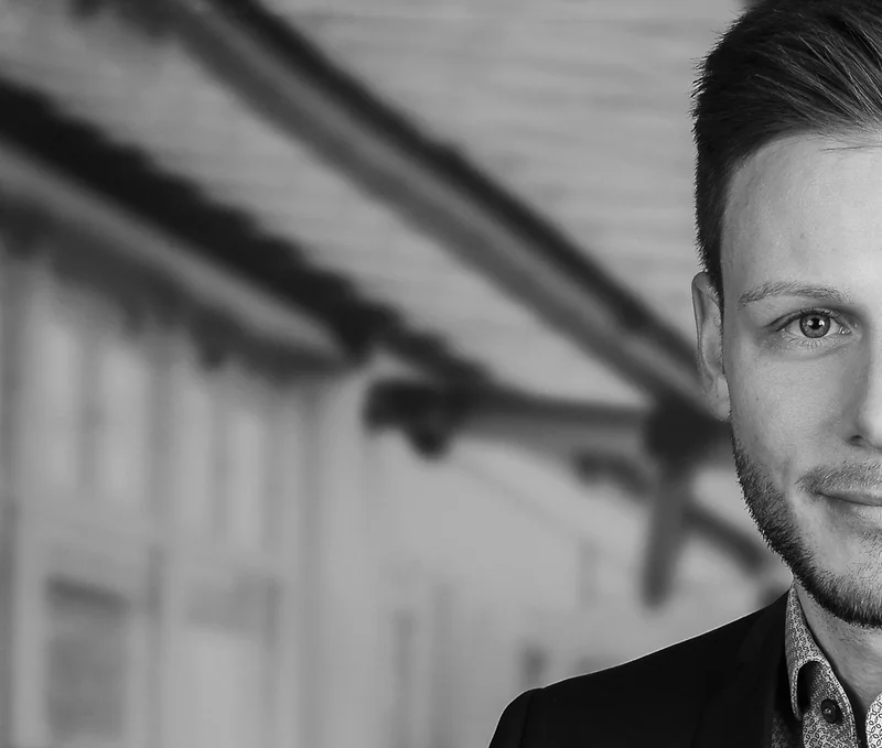 Schwarz-Weiß-Businessportrait eines Mannes am rechten Bildrand vor unscharfer Architektur