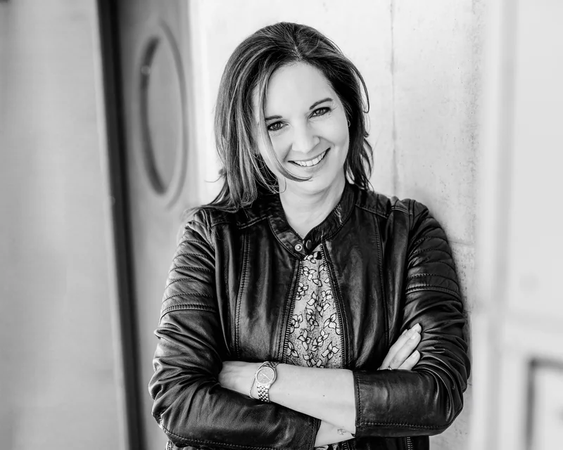 Anne Simon lehnt lächelnd mit verschränkten Armen an einer Wand